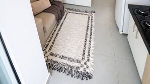 Et kompakt køkken med hvide skabe, en indbygget komfur og et spiseområde med en sofa og et tæppe.