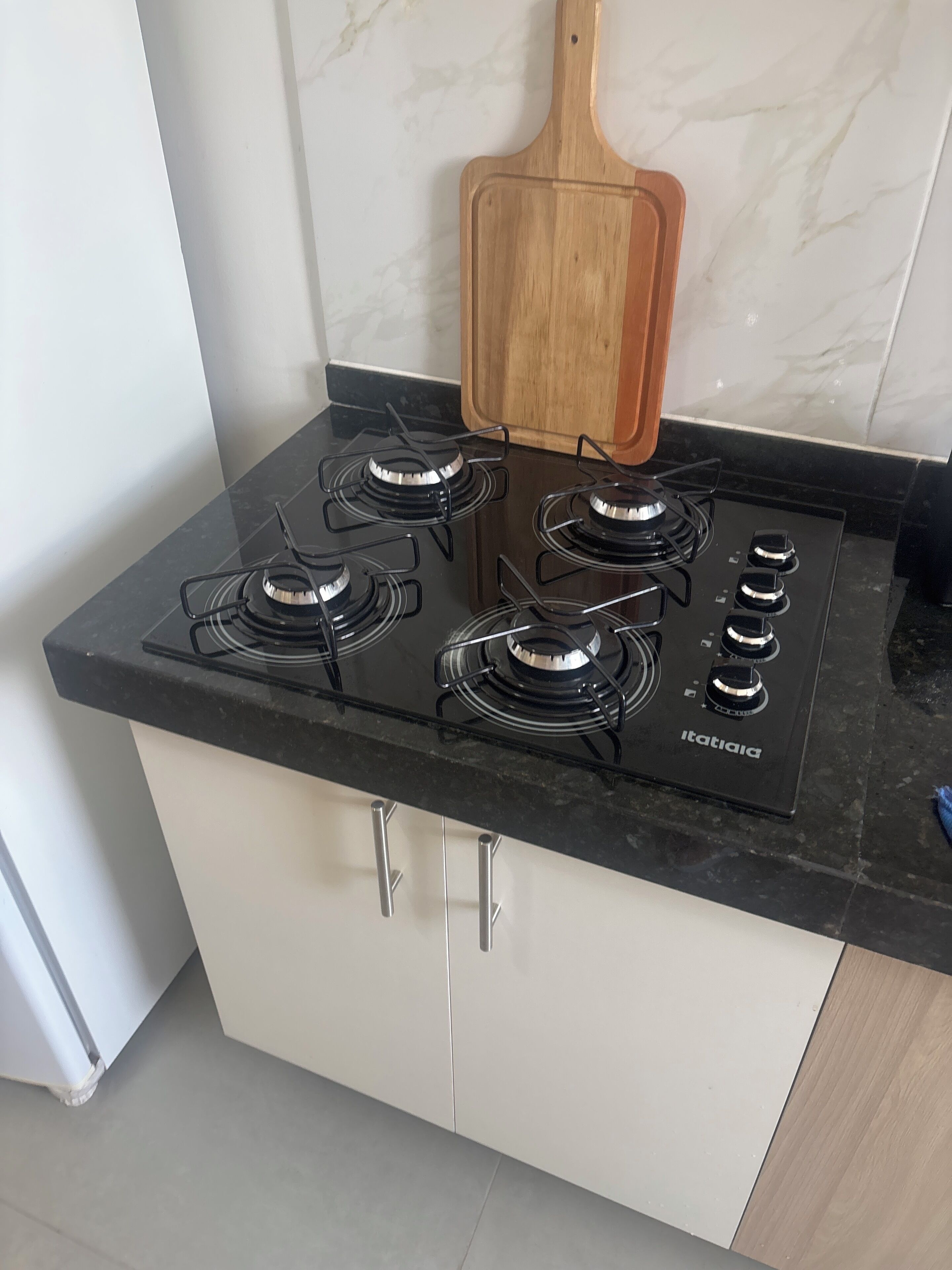 A kitchen with a black gas stove, four burners, and a wooden cutting board on the countertop.