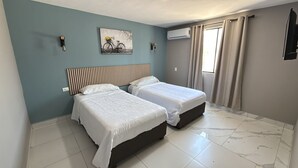 Una habitación con dos camas, aire acondicionado en la pared y una ventana con cortinas.