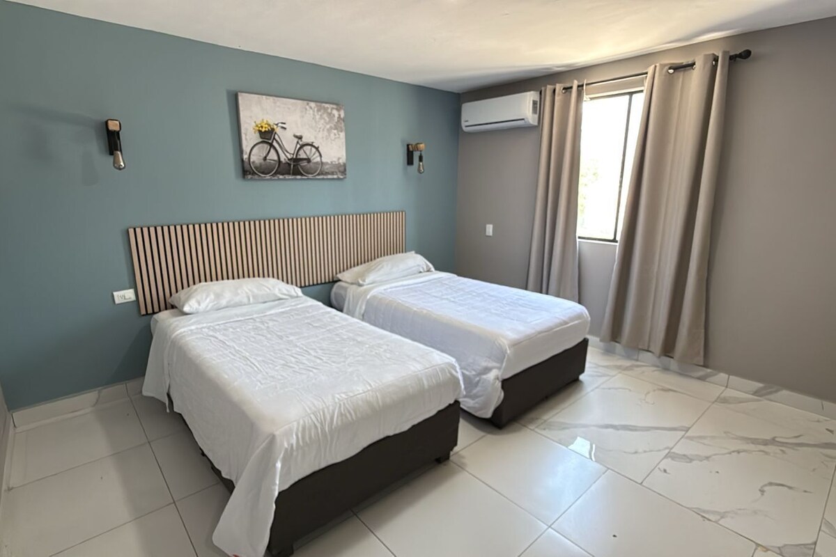 A room with two beds, a wall-mounted air conditioner, and a window with curtains.