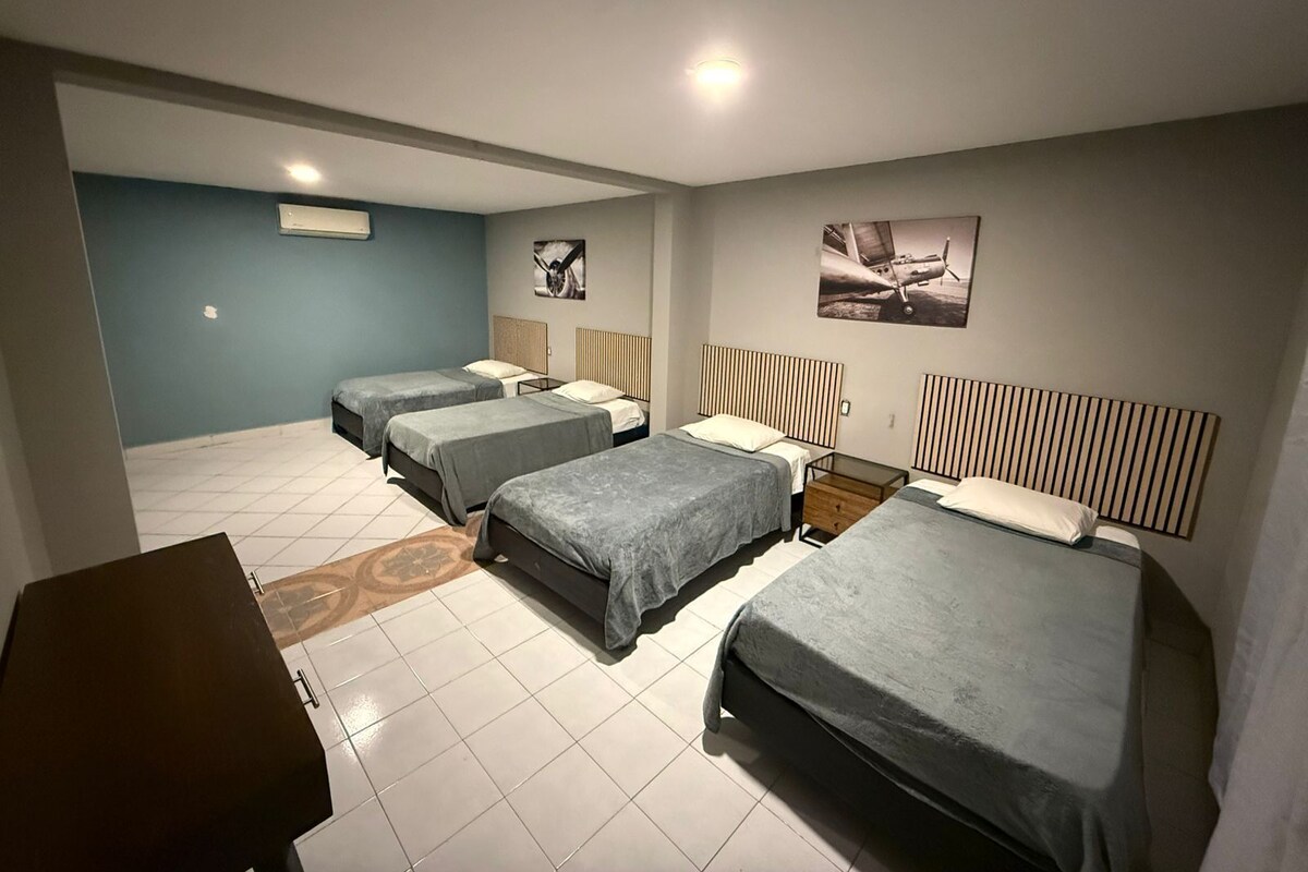 A hotel room with four beds, a small table, and a ceiling light.