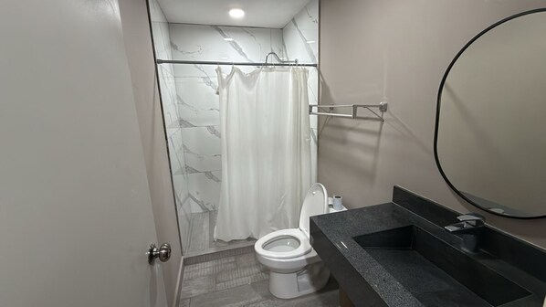 Een badkamer met douche, toilet en wastafel.