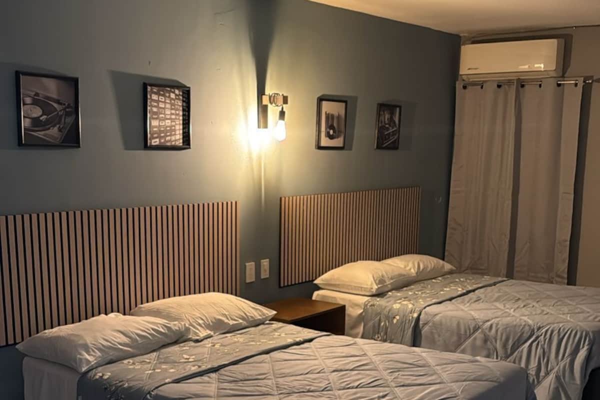 A hotel room with two beds, a wall-mounted air conditioner, and a light fixture.