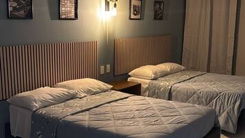 Quarto de hotel com duas camas, ar condicionado fixado na parede e luminária.