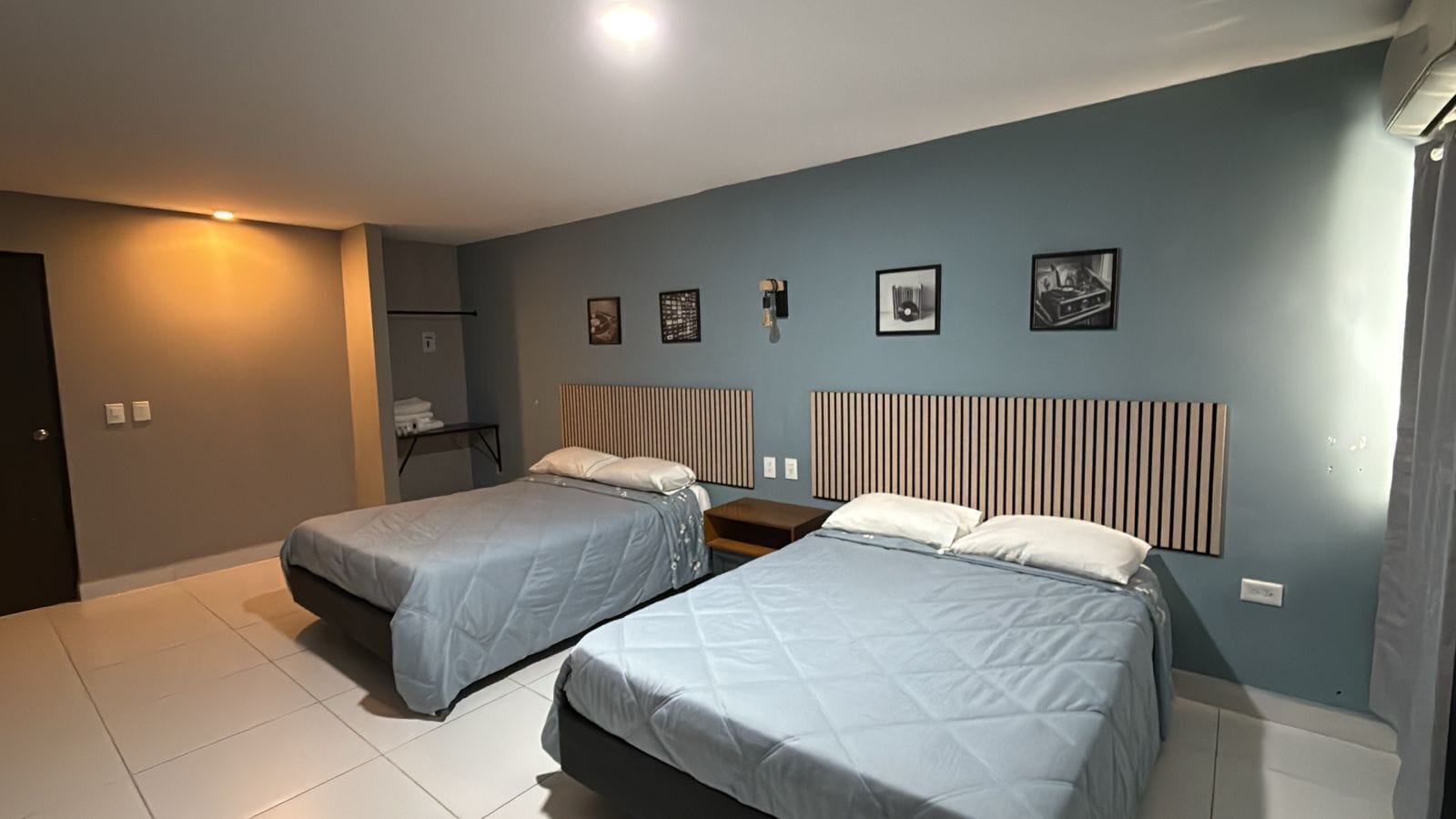 Un dormitorio con dos camas, una mesita de noche, una lámpara de pared y un estante pequeño con un marco de fotos.