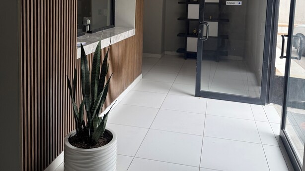 Zona de recepción con pared de paneles de madera, una planta en maceta, un cartel de prohibido fumar y un puerta de cristal que da a una habitación.