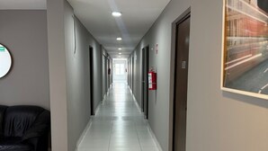 Un pasillo de hotel con un sofá de cuero negro, pisos de baldosas blancas y puertas a ambos lados.