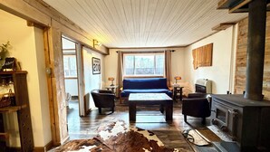 Ein gemütliches Wohnzimmer mit einem großen Fenster, einem blauen Sofa, einem Holztisch und einem Kamin.