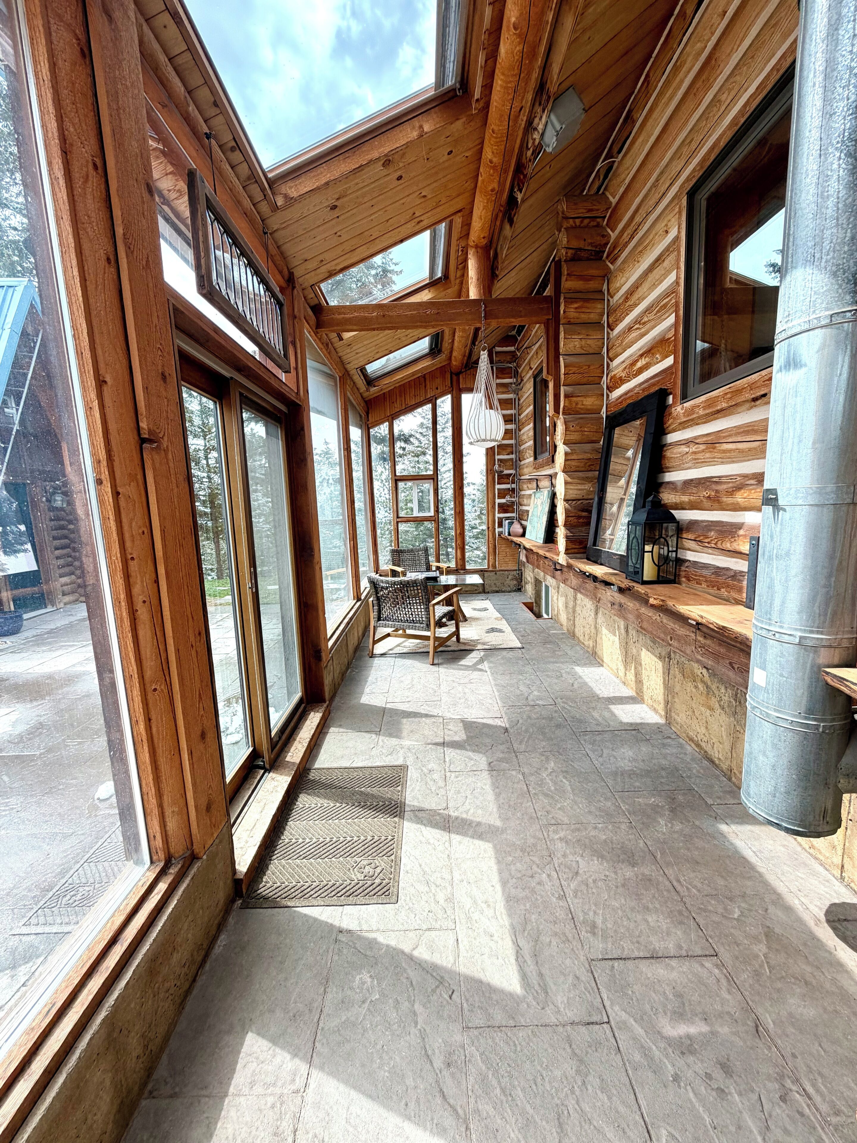 A log cabin interior with large windows, a stone floor, and a bench.