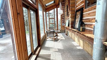 A log cabin interior with large windows, a stone floor, and a bench.
