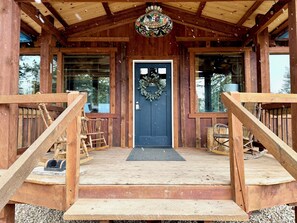 A wooden cabin with a front porch, a door with a wreath, and a hanging light fixture. - Ridgeline Retreat - Fall Mountain Escape - Valley View + Fire Pit (Missoula)