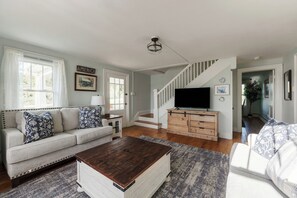 A living room with a sofa, coffee table, TV, staircase, and a door leading to another room.
