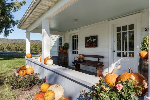 A porch with a bench, pumpkins, and a welcome sign.