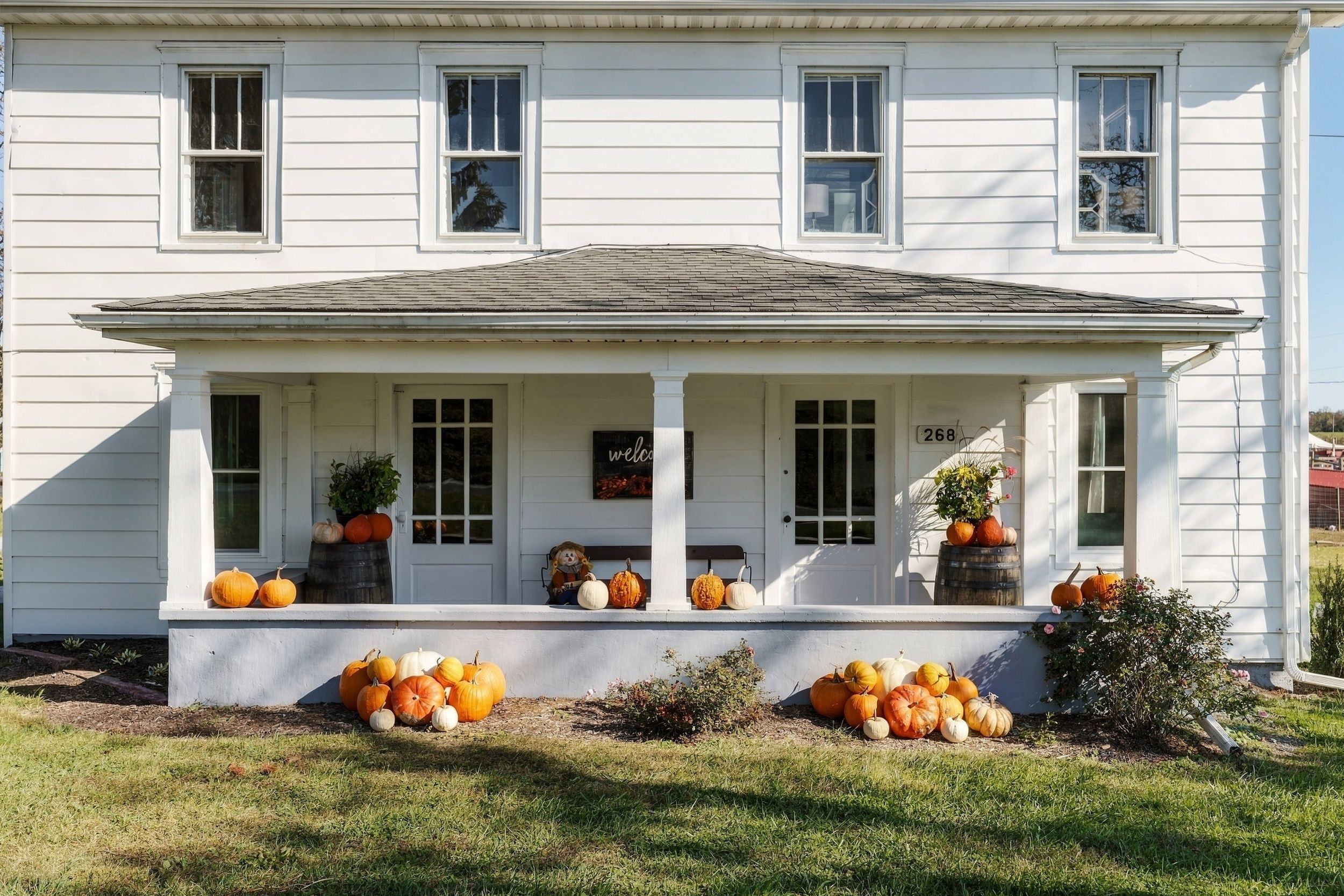 Une maison blanche à deux étages, dotée d’un porche, portant le numéro 268, et décorée de citrouilles et d’un épouvantail.