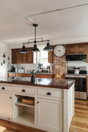 A kitchen with a central island, wooden cabinets, a brick accent wall, and modern appliances.