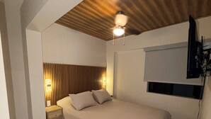 Un dormitorio con cama, techo de madera, televisor montado en la pared, lámparas de noche y suelo de mármol.