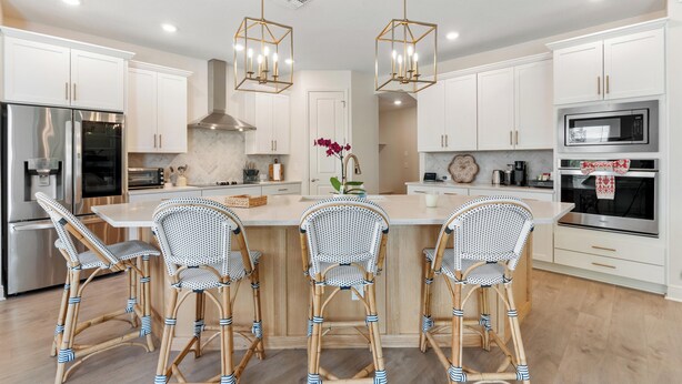 Una cocina moderna con armarios blancos, una isla central con taburetes de bar, electrodomésticos de acero inoxidable e iluminación colgante.