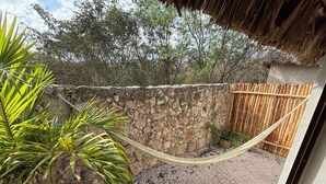 Een hangmat bevestigd tussen een stenen muur en een houten hek in een tuin met grind en tropische planten.