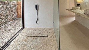 Een moderne badkamer met een stenen vloer, een douchecabine van glas, een houten plafond en een stenen wand.
