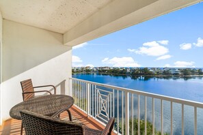 Un balcón con mobiliario de mimbre con vista a un lago tranquilo y una zona residencial.
