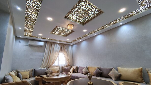 Un soggiorno moderno con un divano, un tavolino in vetro e pannelli decorativi a soffitto.