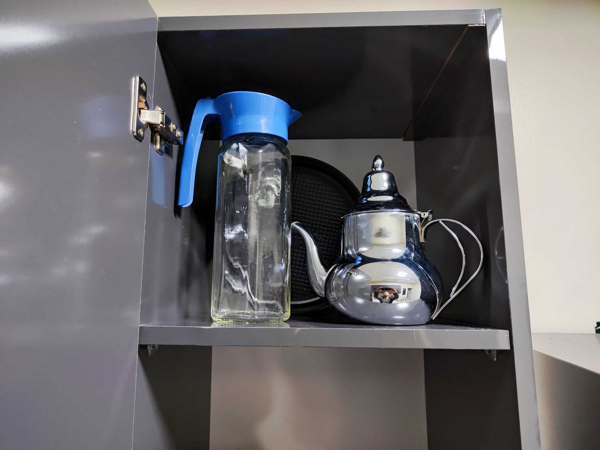 Un meuble métallique contenant une bouteille d’eau bleue et une bouilloire argentée.