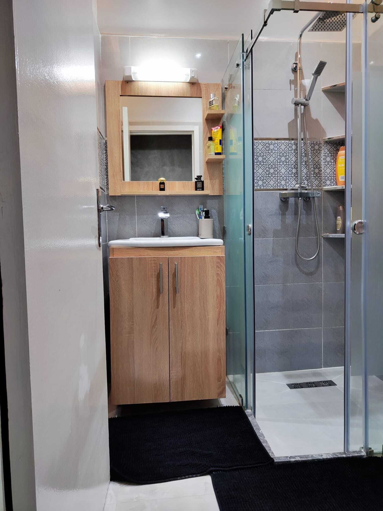 A modern bathroom with a wooden vanity, a glass shower enclosure, and a tiled backsplash.