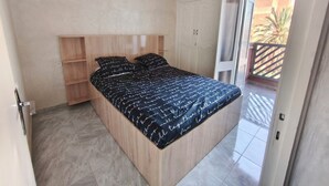 Camera da letto con un letto, una testata in legno, scaffali a muro, un armadio e un balcone con vista.