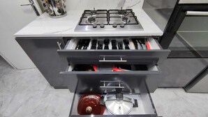 Una cucina con piano cottura a gas, un cassetto con utensili e una pentola rossa.