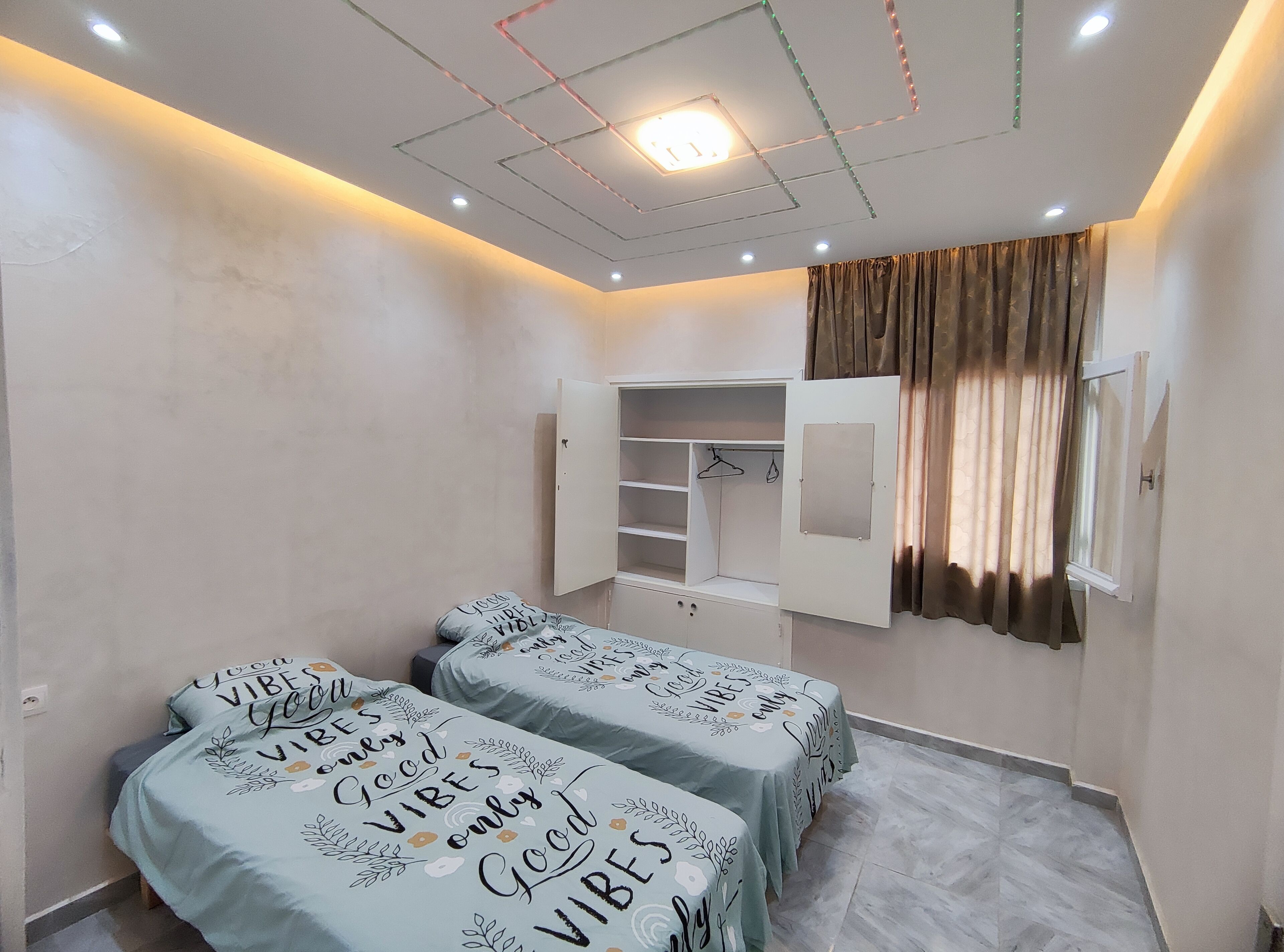 A bedroom with two beds, a wardrobe, and a window with curtains.