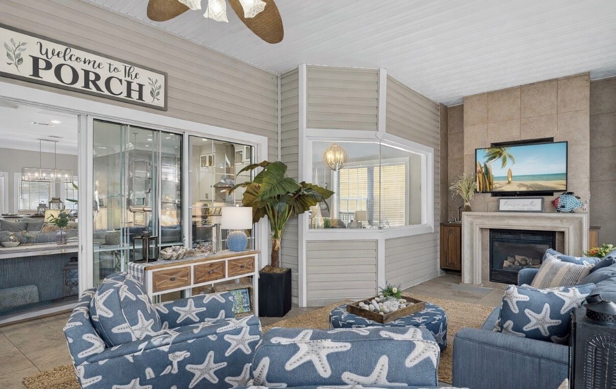 A living room with a large window, a television, a fireplace, and a sign that reads "Welcome to the PORCH".