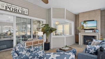 A living room with a large window, a television, a fireplace, and a sign that reads "Welcome to the PORCH".