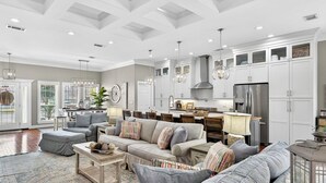 A spacious living room with a large sofa, a coffee table, and a dining area with a kitchen in the background. - Golf Cart - Pool - Walk to Beach - Fully Remodeled - Crystal Beach - Sleeps 10 (Destin)