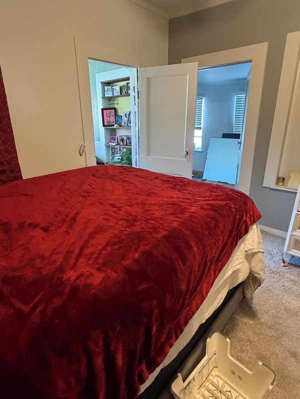 A bedroom with a red bedspread, a white door, and a white dresser.