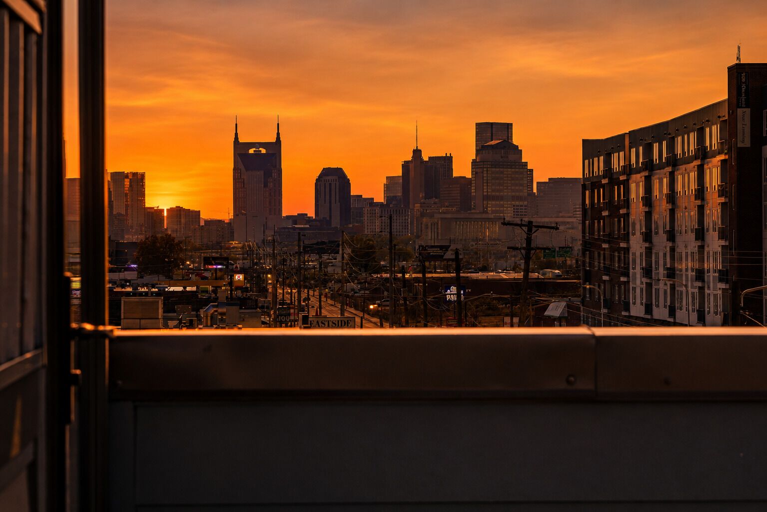 A city skyline at sunset with high-rise buildings, including a distinctive building with a pointed top.