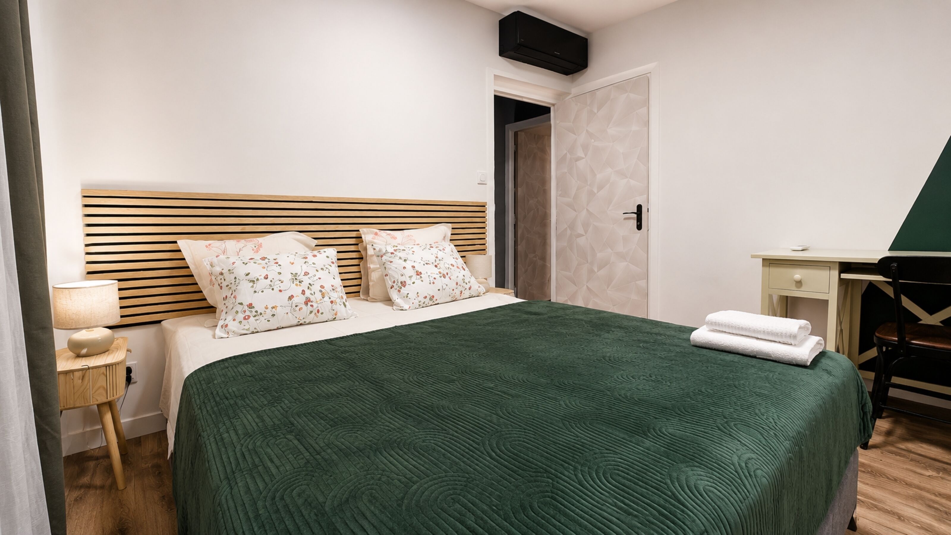 A neatly arranged hotel room with a bed, bedside table, lamp, and a desk with a chair.