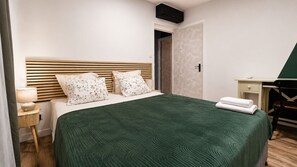 A neatly arranged hotel room with a bed, bedside table, lamp, and a desk with a chair. - Le Cocon des Romarins – 3 bedrooms, air conditioning, balcony, and shared pool (Montélimar)
