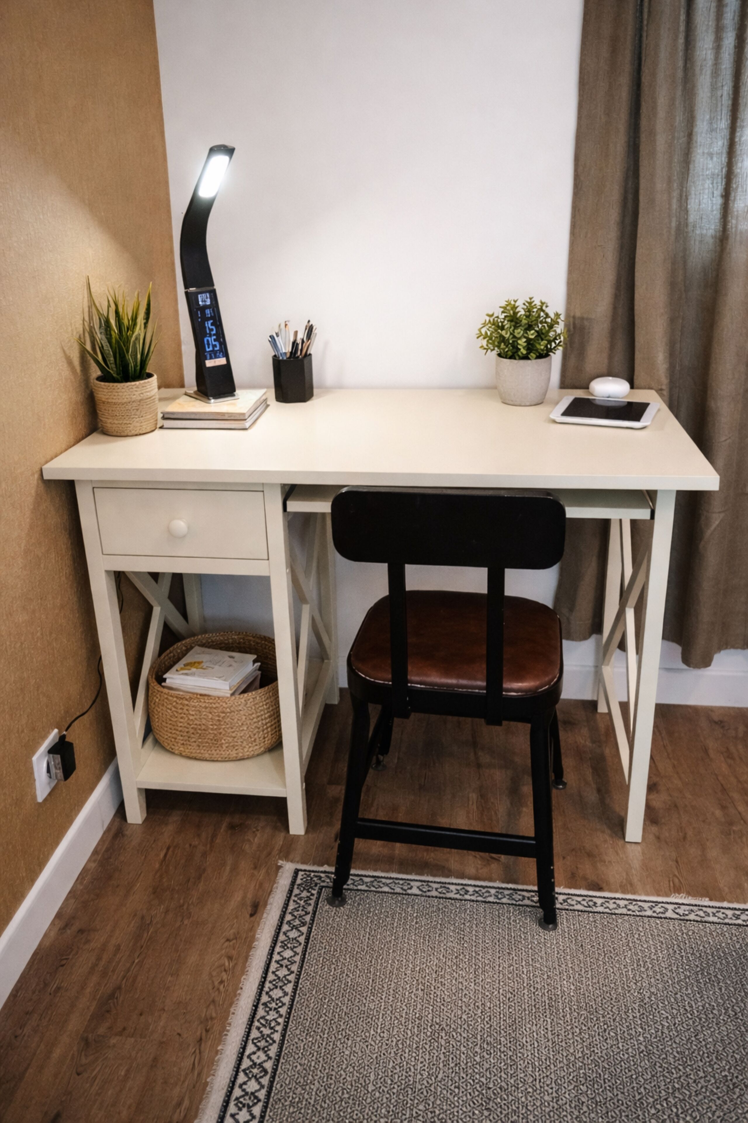 A white desk with a black chair, a desk lamp, a potted plant, and a tablet.