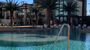 Una piscina amb una escala metàl·lica, palmeres i un edifici modern amb grans finestres al fons.
