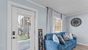 A living room with a blue sofa, a clock on the wall, and a door leading to a balcony. - Foley Riverfront Escape Kayaks Firepit Near Beach (Foley)