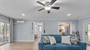 A spacious living room with a blue sofa, wooden flooring, and a ceiling fan. - Foley Riverfront Escape Kayaks Firepit Near Beach (Foley)