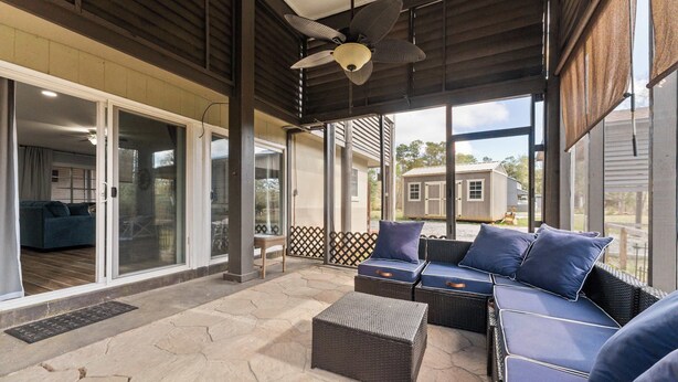 An outdoor patio with wicker furniture, a ceiling fan, and large windows offering a view of the surrounding area. - Foley Riverfront Escape Kayaks Firepit Near Beach (Foley)