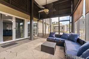 Une terrasse extérieure aménagée avec des meubles en osier, un ventilateur de plafond et de grandes fenêtres offrant une vue sur les environs.