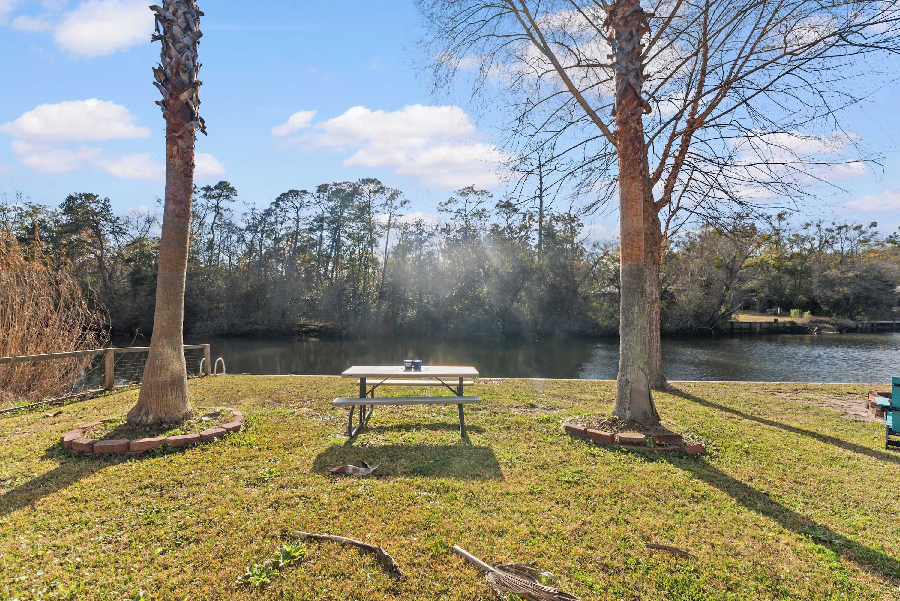 A picnic table surrounded by grass and trees, overlooking a calm body of water.