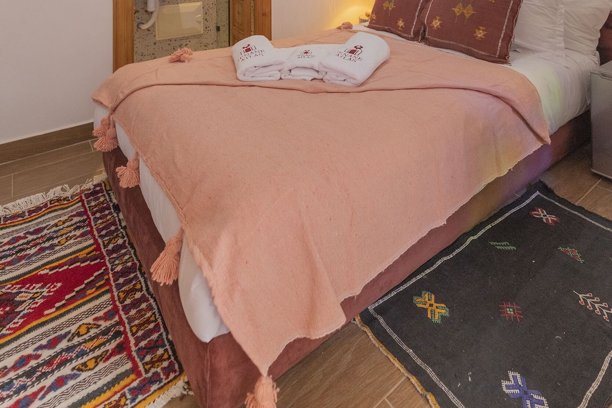 A bedroom with a bed, a wall-mounted air conditioner, a decorative ceiling light, a wooden door, and a small wall-mounted mirror.