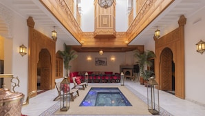 A luxurious lobby with a central pool, ornate wooden arches, and a seating area with red cushions. - Riad Jnane Zephyr (Marrakech)