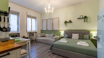 Une chambre à coucher comprenant un lit, des tables de chevet, un lustre, une fenêtre et un coin cuisine.