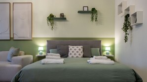 Un dormitorio ordenado con cama, mesitas de noche, una silla y estanterías con plantas.