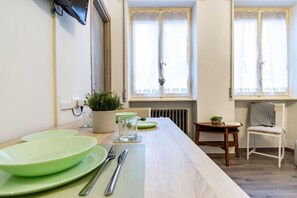 Ein Essbereich mit einem langen Tisch, grünen Tellern, Besteck, einem Blumentopf und einem Stuhl.