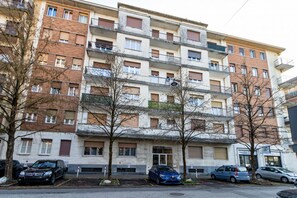 Un edificio residencial de varios pisos con balcones, coches aparcados y árboles sin hojas.